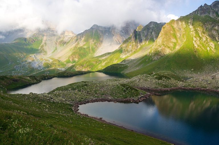 A turquoise glacier lake nestled in a green mountain valley beneath rocky peaks.